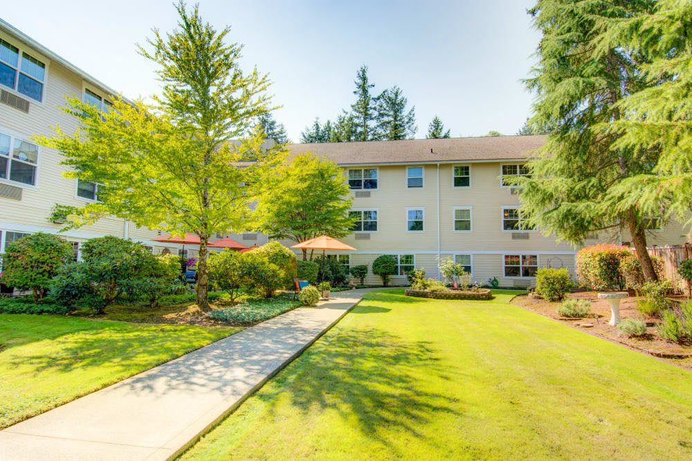 A sunny view of a residential apartment building surrounded by a landscaped garden with trees and a well-maintained lawn.
