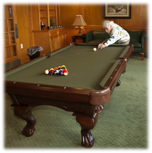 A person aiming at the cue ball on a pool table in a cozy room.