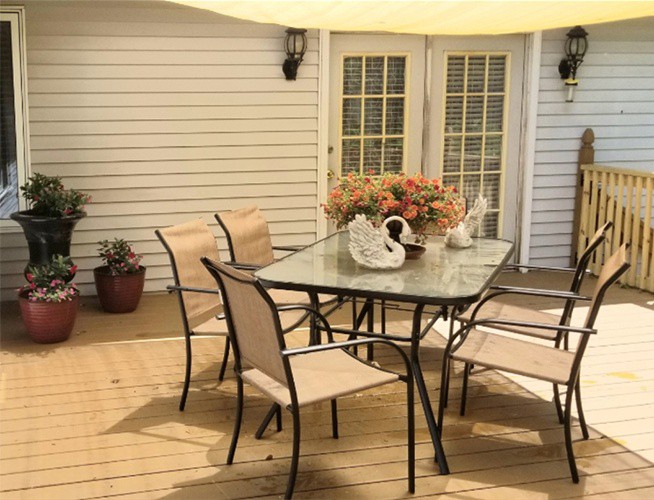 A cozy outdoor patio with a glass table, chairs, and decorative plants.