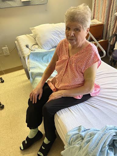 A woman sitting on the edge of a hospital bed, dressed in casual clothing.