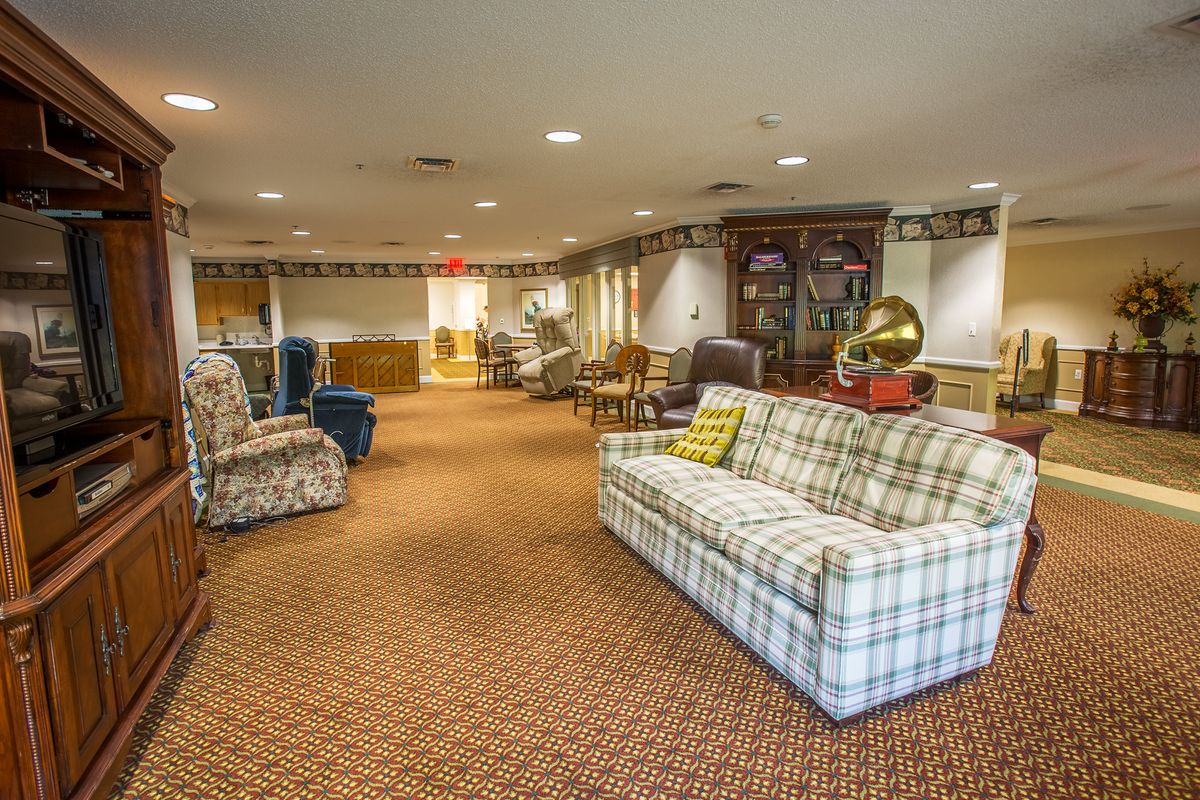 A spacious living room with comfortable seating, featuring a plaid sofa, armchairs, a gramophone, and a bookshelf.