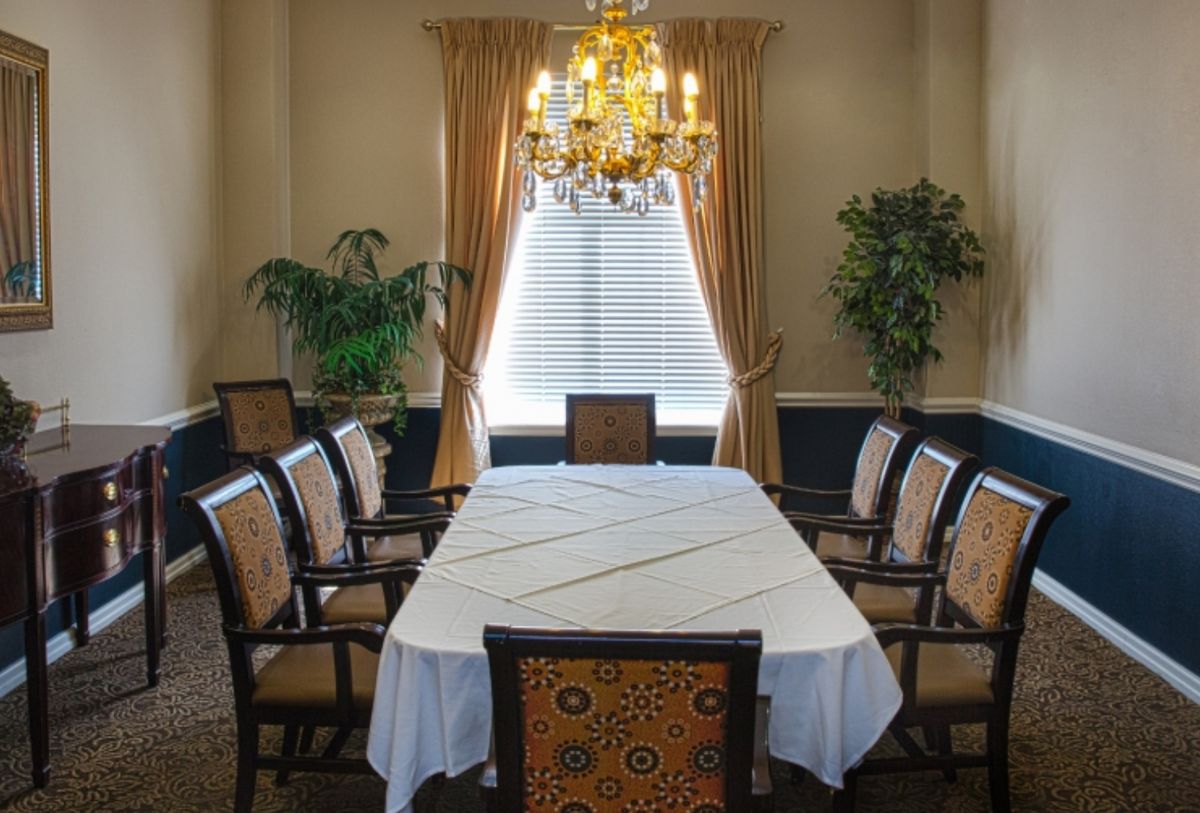 A formal dining room with a long table, surrounded by chairs, adorned with a chandelier and elegant curtains.