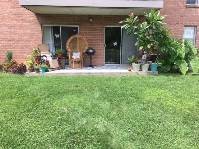 A cozy patio area with chairs and various potted plants, adjacent to a well-maintained lawn.