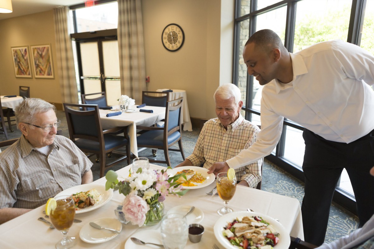 A waiter serves food to an elderly couple in a restaurant setting.