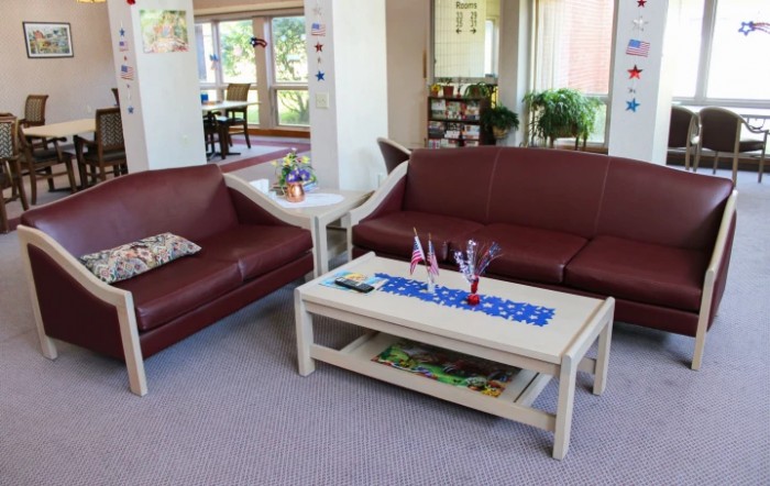 A cozy living room with two leather sofas and a coffee table, decorated with flowers and houseplants.