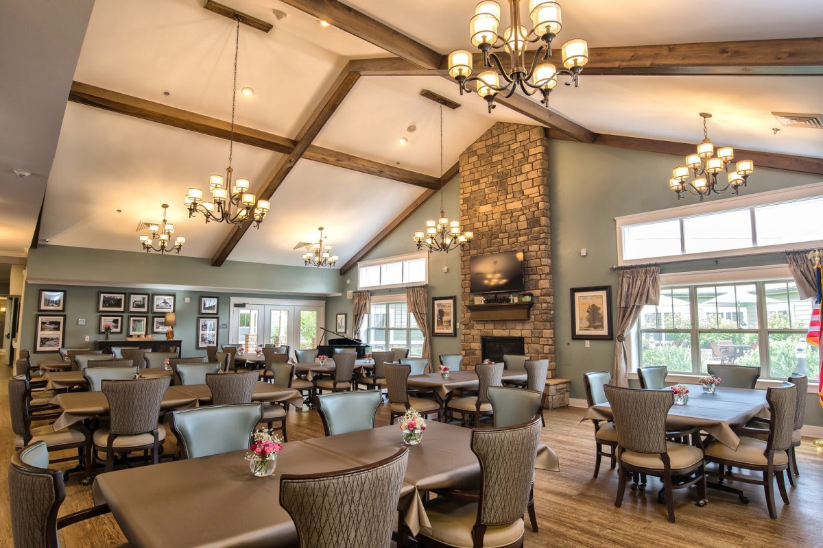 A spacious dining room with elegant chandeliers, a stone fireplace, and comfortable seating.
