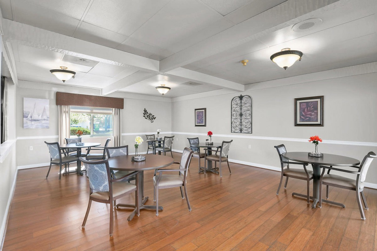 A spacious dining area with multiple tables and chairs, featuring a hardwood floor and decorative wall art.