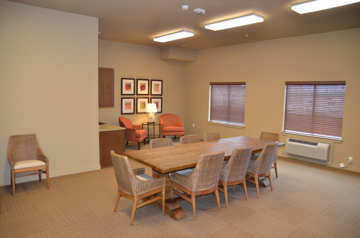 A modern conference room featuring a large wooden meeting table surrounded by chairs, with artwork adorning the walls and ample overhead lighting.