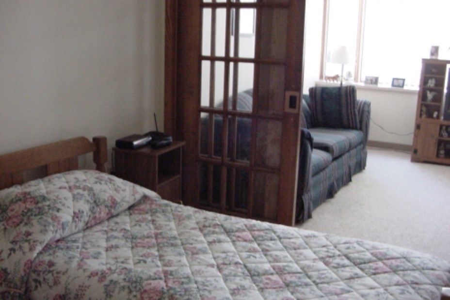 A cozy bedroom with a quilted bedspread and a small sofa seen through wooden sliding doors.