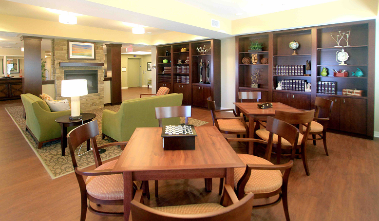 A modern lounge area featuring wooden tables and chairs, a bookshelf, and comfortable seating.