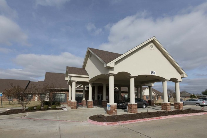 A large building with a covered entrance, featuring columns and a driveway under a partly cloudy sky.