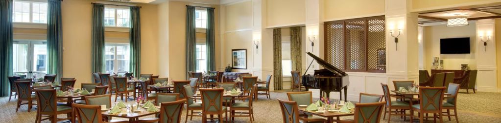 A spacious dining area with neatly arranged tables and chairs, featuring a piano in the corner.