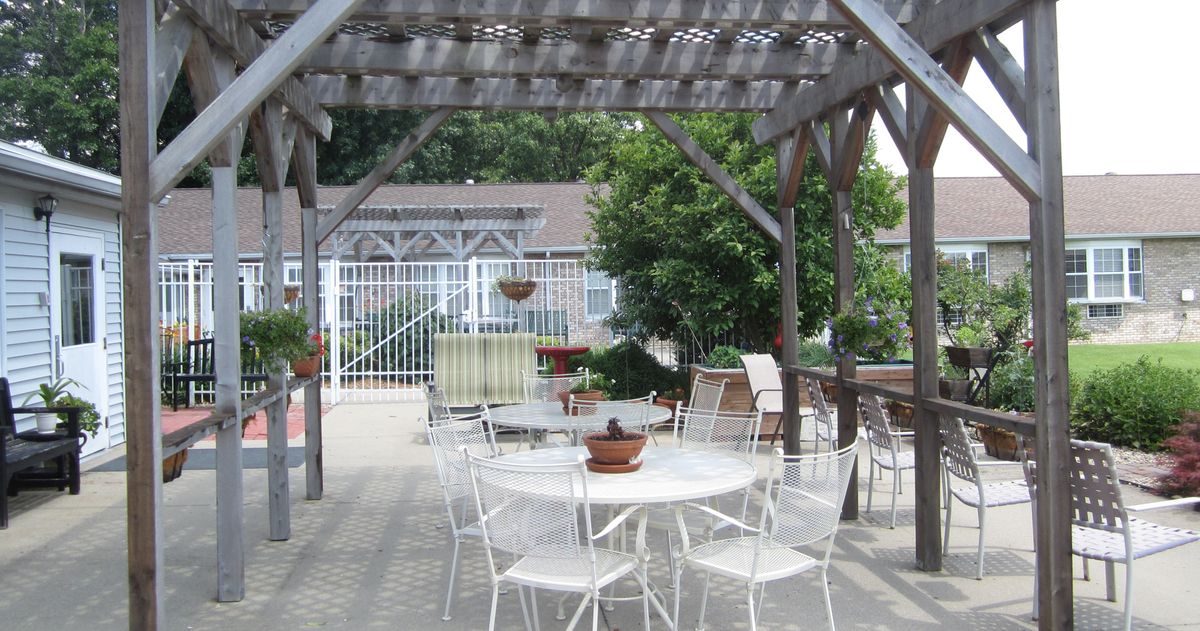 A peaceful patio area with a pergola, featuring white garden furniture and potted plants.