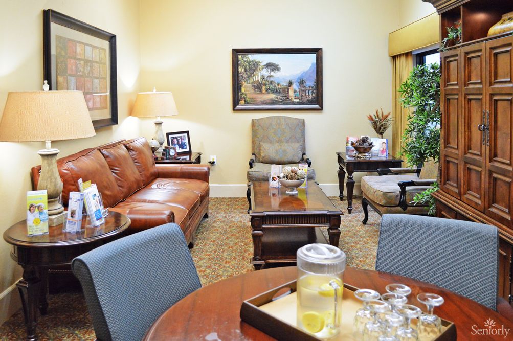 A cozy living room with a leather sofa, armchairs, and a coffee table. The walls are adorned with paintings and theres a tray with lemonade on the table.
