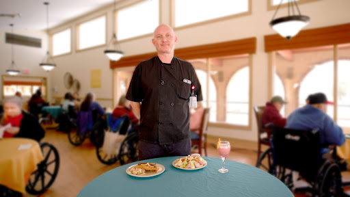 A chef proudly presents two beautifully plated meals in a welcoming dining area.