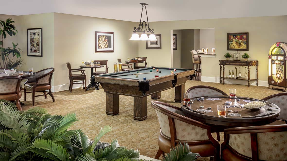 A cozy recreation room featuring a pool table and comfortable seating areas with framed art on the walls and elegant lighting.