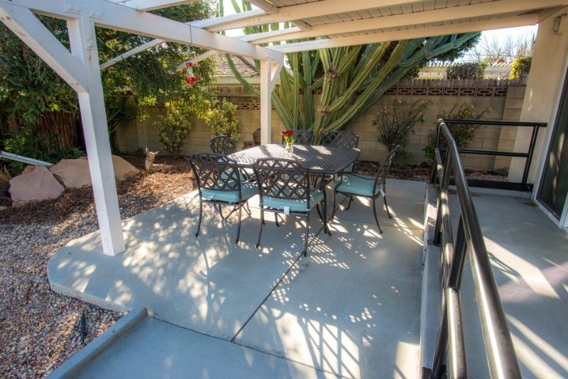 A cozy outdoor patio area with a table and chairs under a pergola, surrounded by garden plants.