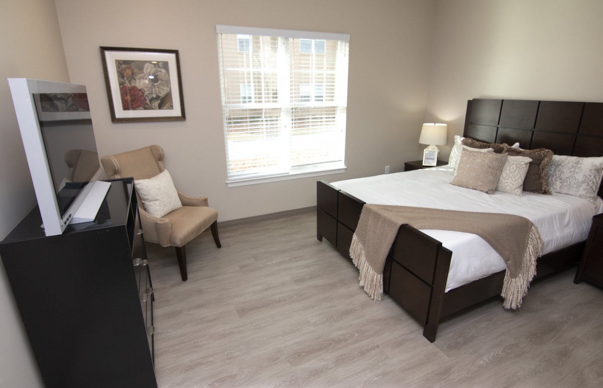 A cozy bedroom featuring a neatly made bed, a comfortable chair, and a large window allowing natural light to brighten the space.