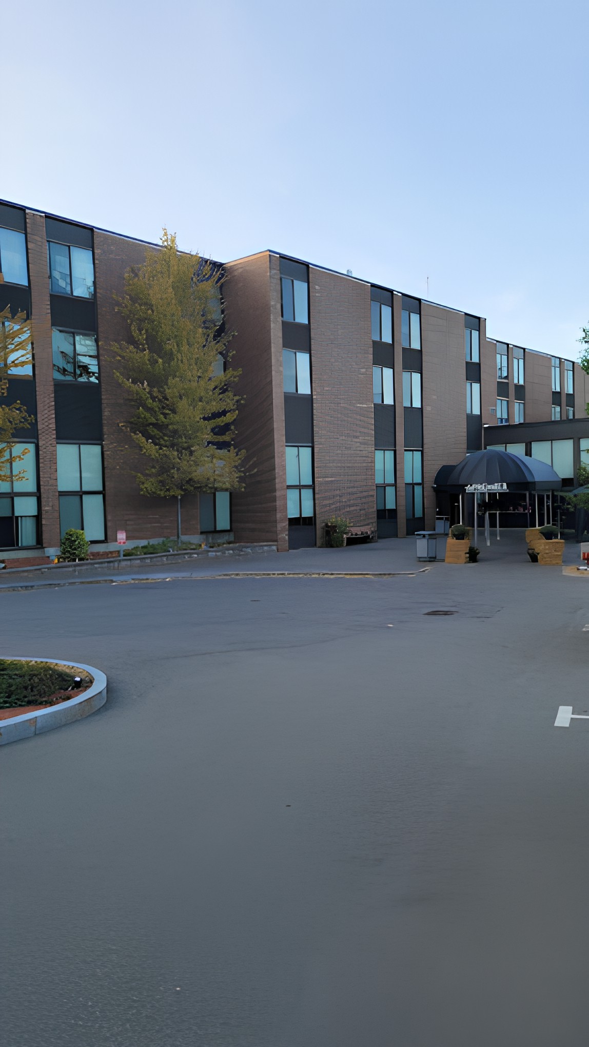 A modern hotel building with a spacious parking lot and surrounding trees.