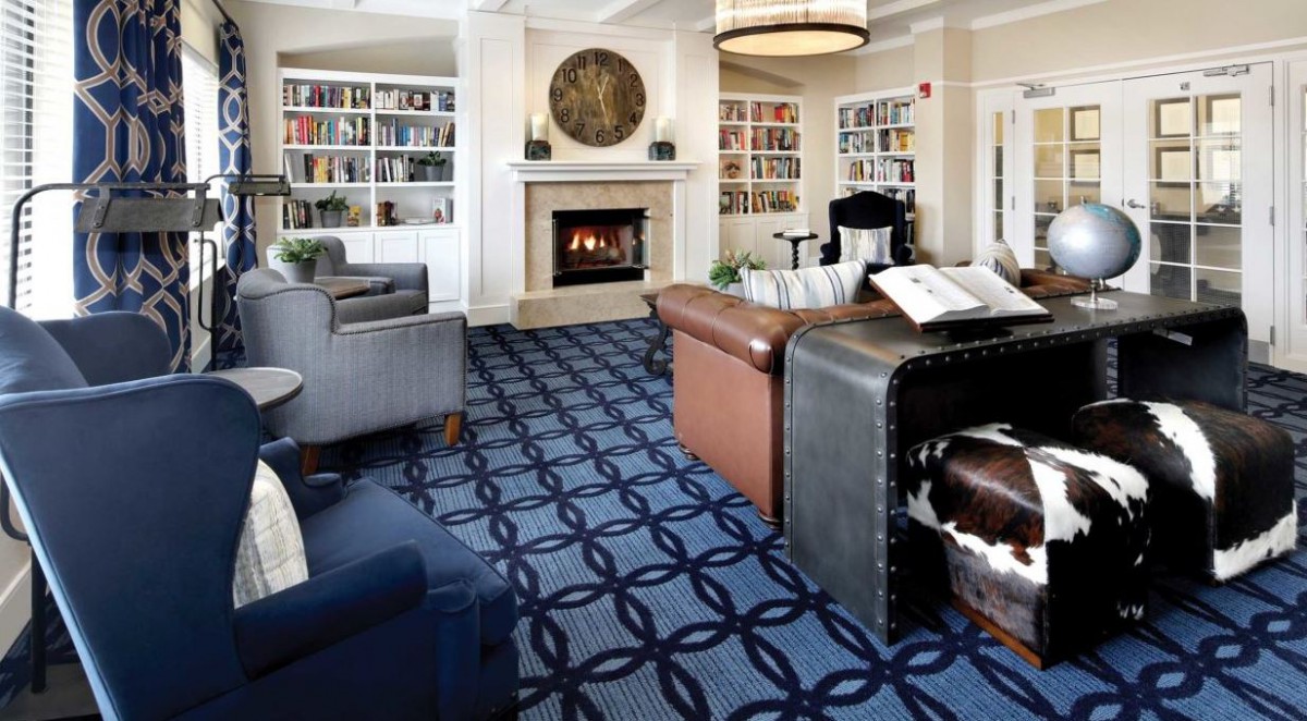 A cozy library room featuring bookshelves, a fireplace, and comfortable seating.