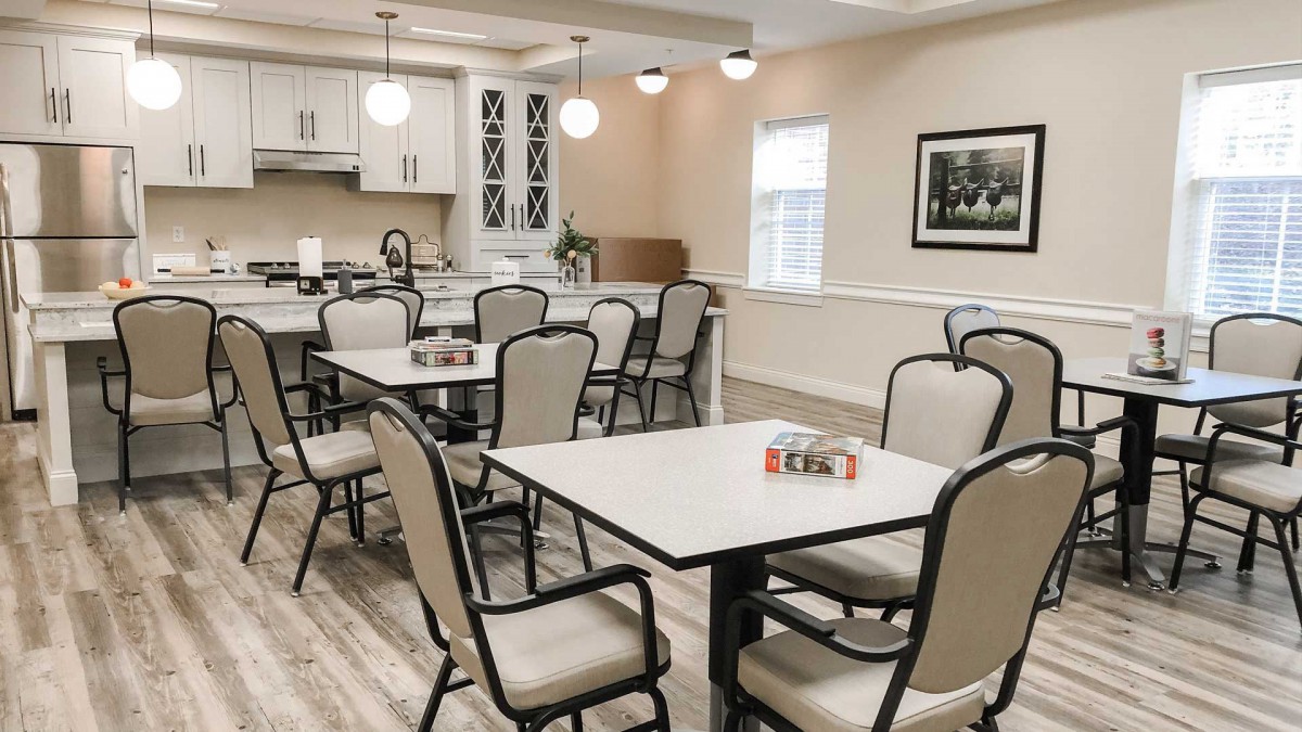 A modern dining area with neatly arranged tables and chairs, featuring a cozy kitchen setup and stylish lighting.