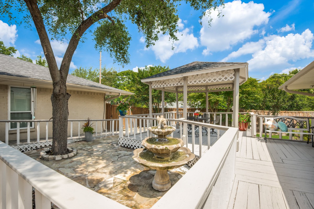 A sunny patio with a fountain and a pergola surrounded by trees.