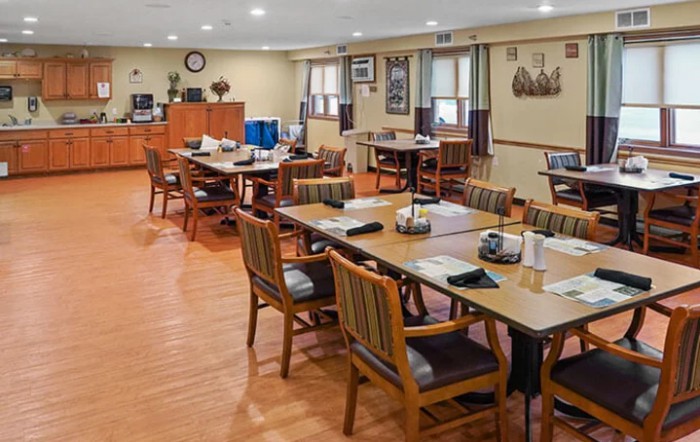 A spacious dining area with neatly arranged tables and chairs on a wooden floor.