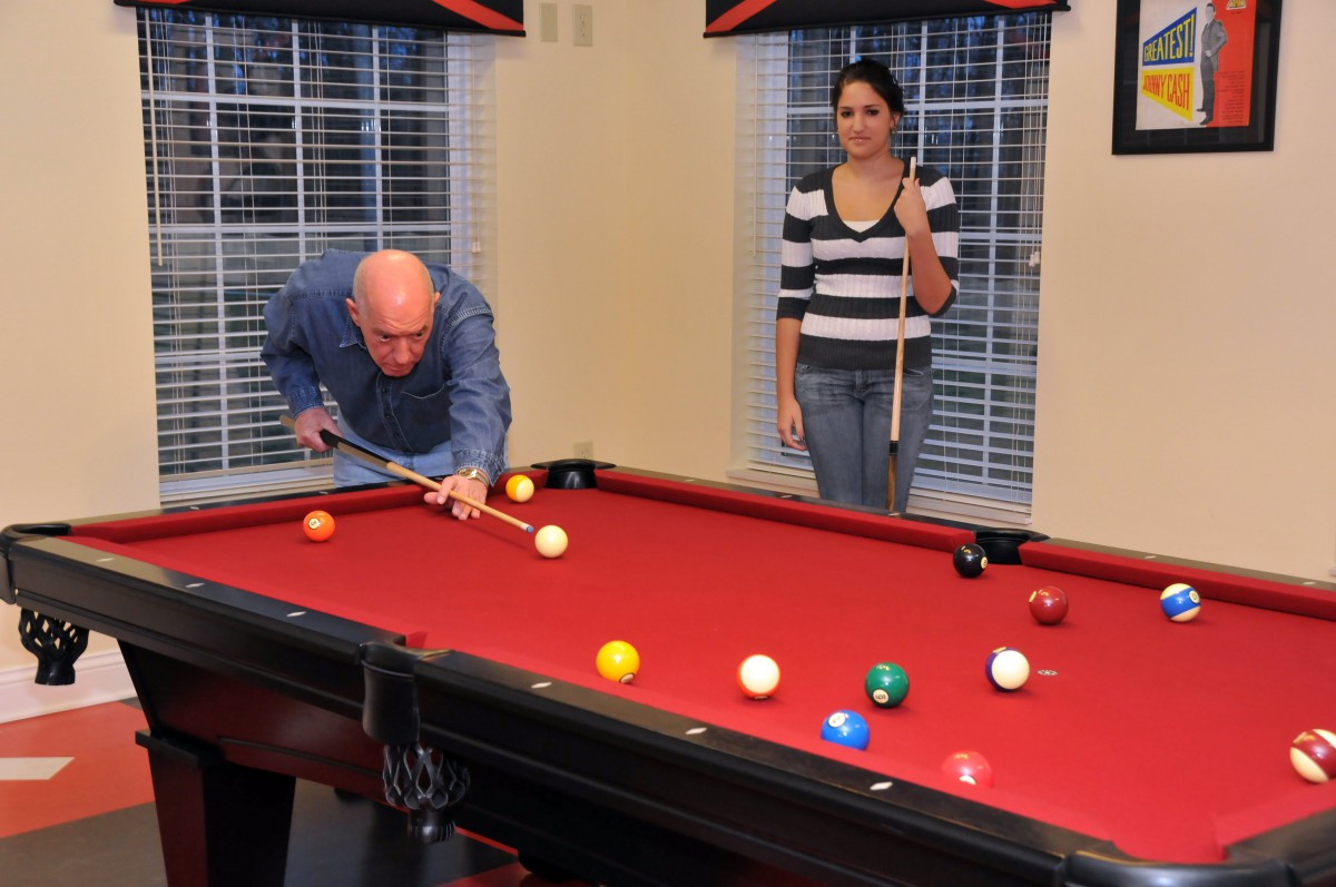 Two people playing a game of pool on a red pool table indoors.