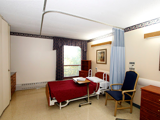 A view of a hospital room featuring a bed, chair, and window.