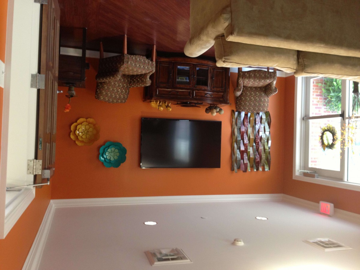 A cozy living room with an orange accent wall featuring a mounted television and decorative wall art.