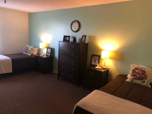 A cozy bedroom featuring a dresser, two lamps, and decorative elements on a light green accent wall.