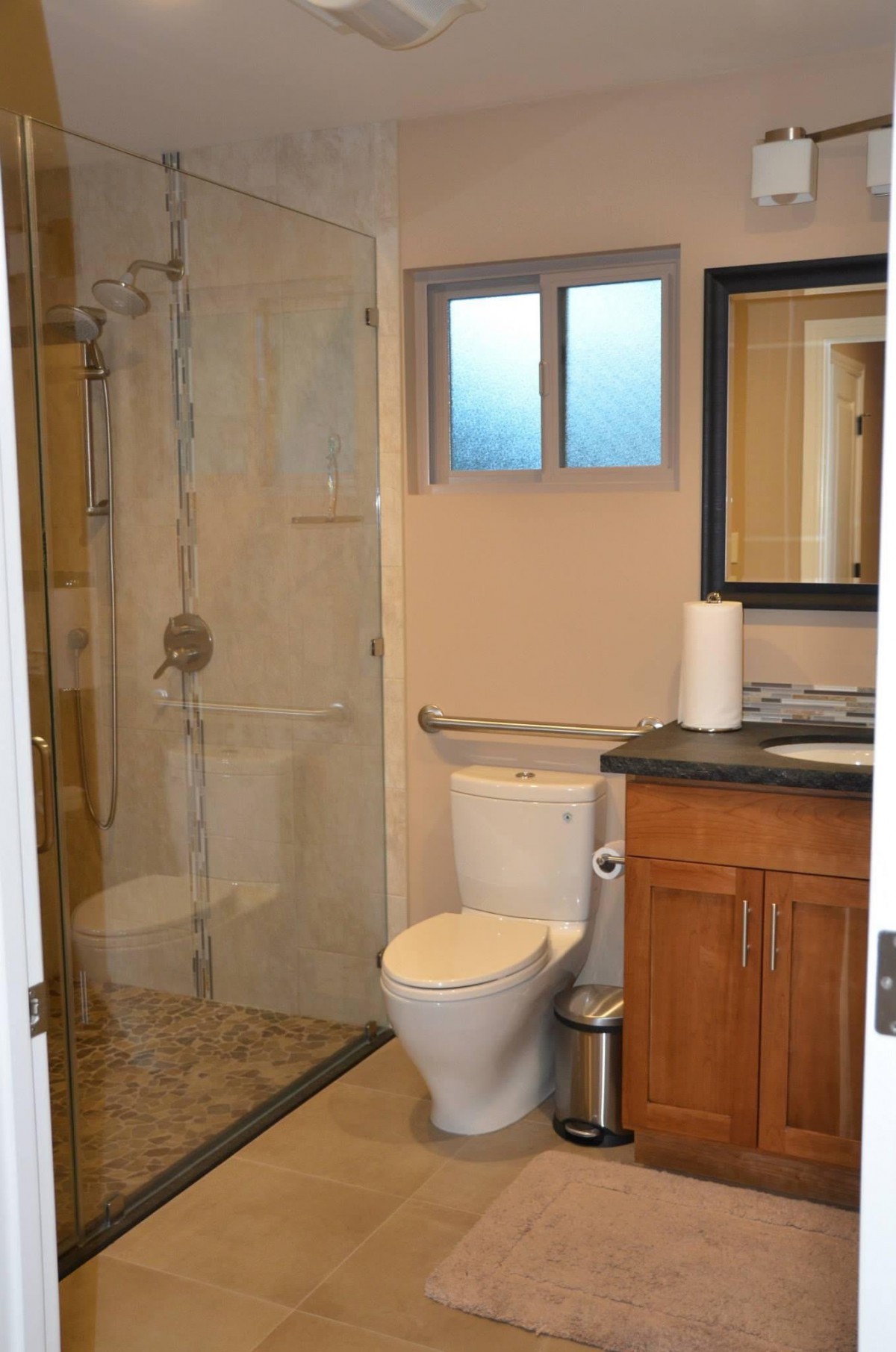 A modern bathroom with a glass shower, toilet, and wooden vanity.