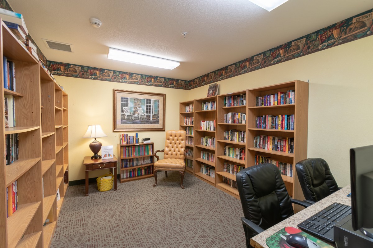 A cozy library room with bookshelves, chairs, and a lamp, creating an inviting atmosphere.