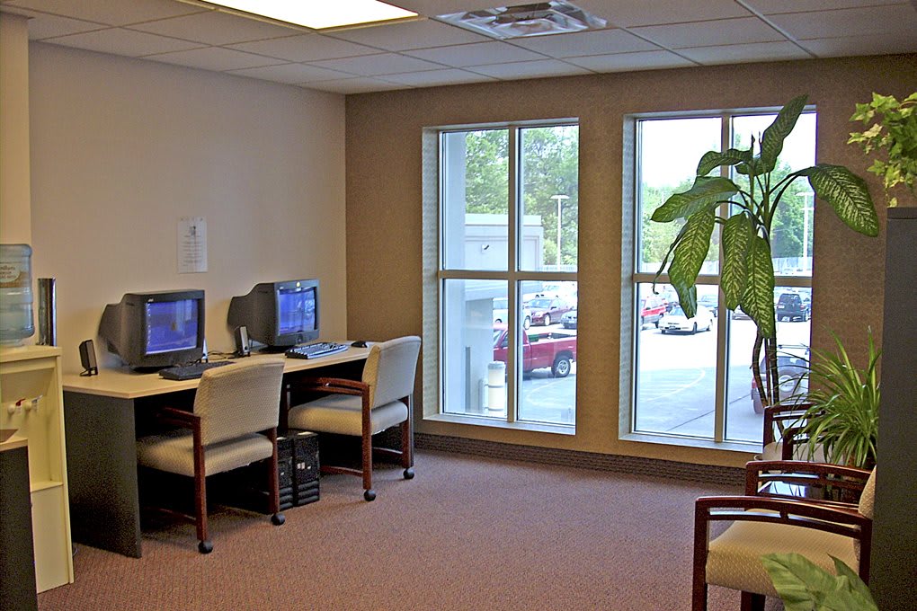 A small office area with two computer stations, chairs, large windows, and an indoor plant.