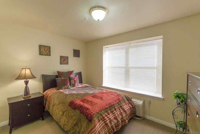 A cozy bedroom with a neatly made bed, wall art, and a large window.