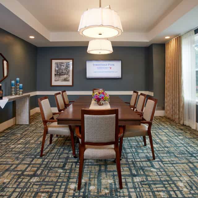 A well-lit conference room featuring a central meeting table surrounded by chairs, with artwork on the walls and decorative lighting overhead.