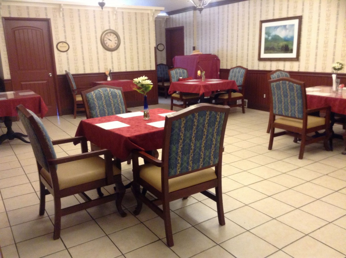 An empty restaurant dining area with neatly arranged tables and chairs, featuring red tablecloths and a wall clock.