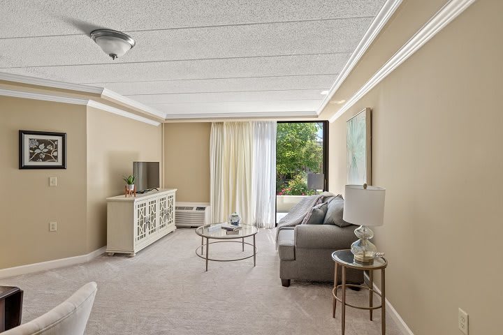 A cozy living room with neutral tones, featuring a sofa, coffee table, and TV stand, with natural light coming through the window.