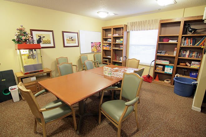 A cozy meeting room with a conference table, chairs, and bookshelves filled with books and games.