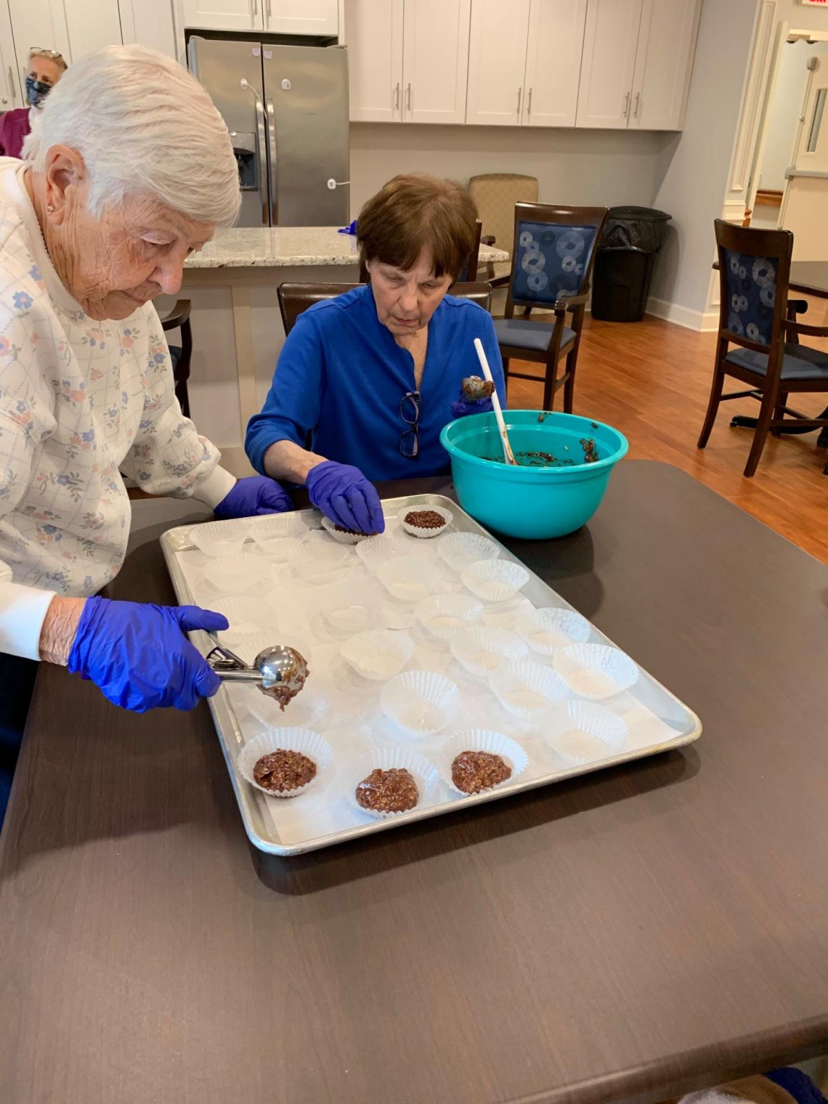 A senior and a child are baking cookies together in the kitchen, placing dough on a tray.