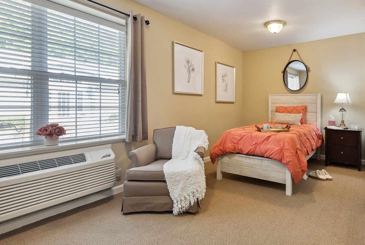 A cozy bedroom with an armchair and a neatly made bed in warm tones.