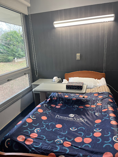 A well-lit hospital room featuring a single bed, a small bedside table, and a window with a view.