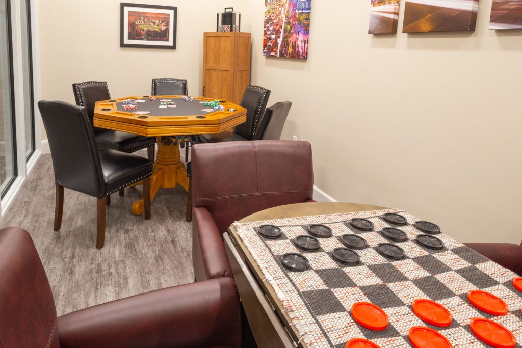 A cozy game room featuring a checkers board setup and a poker table surrounded by chairs.