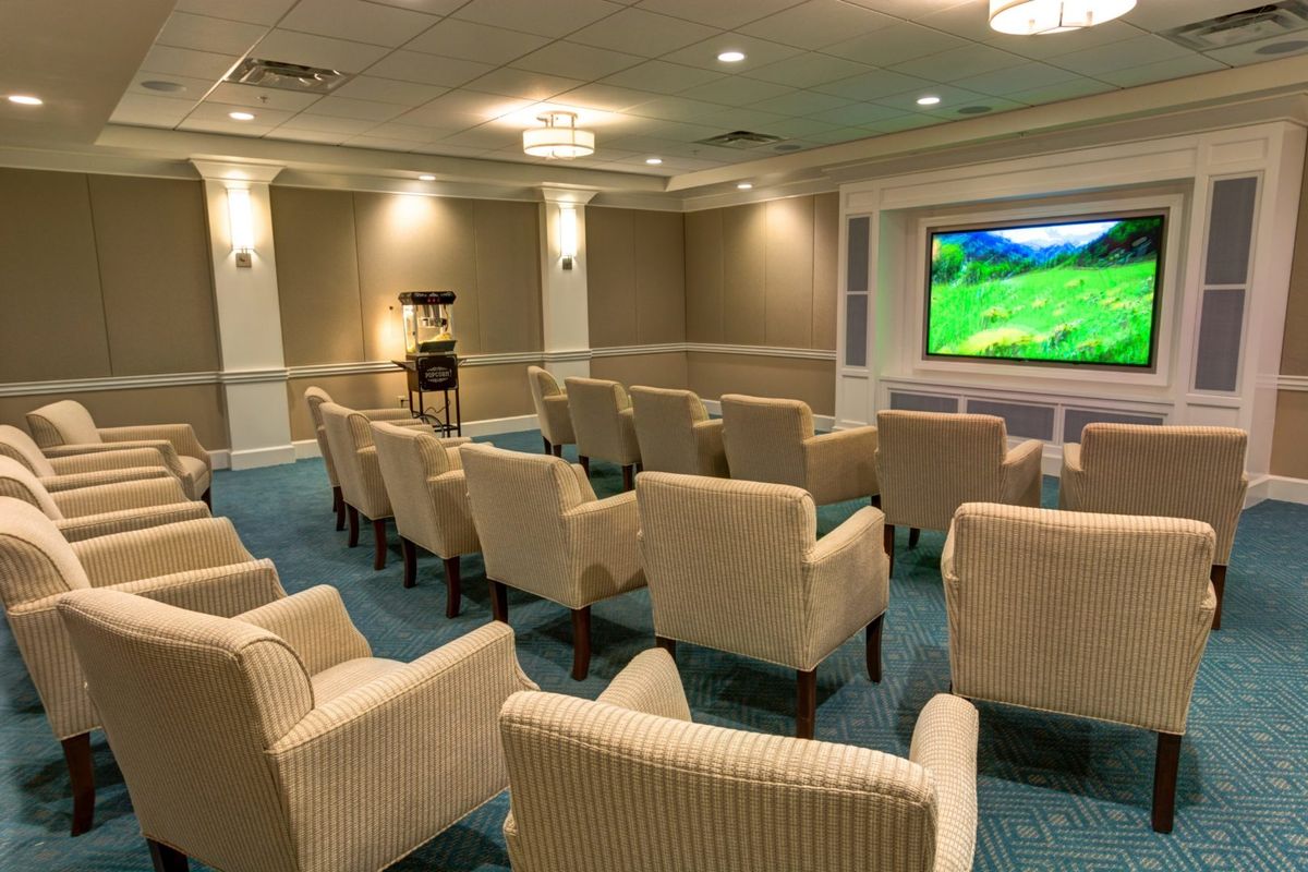A cozy home theater room with multiple rows of comfortable seating facing a large projector screen.
