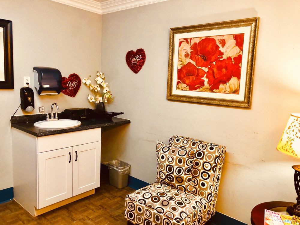 A cozy room featuring a patterned chair, sink area, and floral wall art with heart decorations.