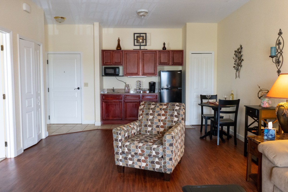 A cozy living space featuring a patterned armchair, a kitchenette with red cabinets, and a small dining area.