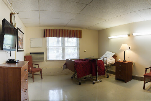 A view of a hospital room featuring a bed, chair, and window with curtains.