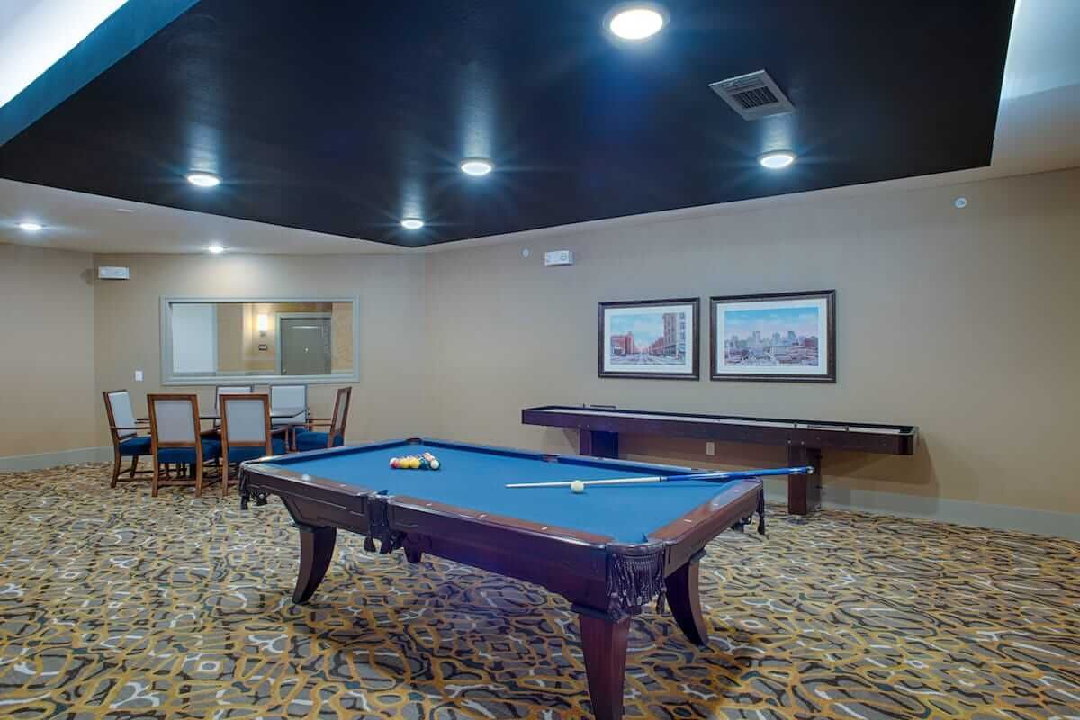 A cozy game room featuring a pool table and carpeted flooring, with ambient lighting creating a relaxed atmosphere.