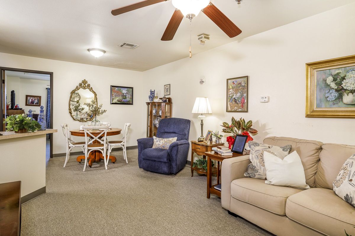 A cozy living room with a sofa, armchair, and dining area, featuring warm lighting and decorative details.