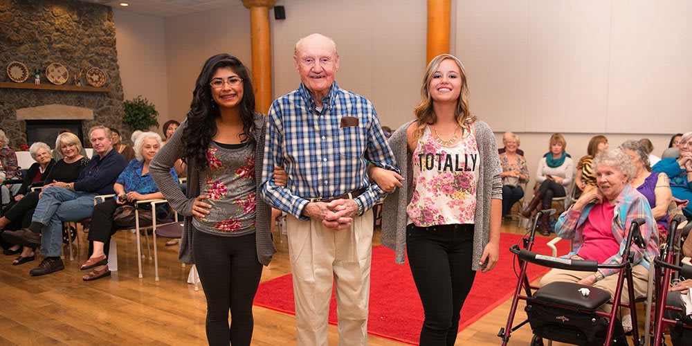 A group of three people smiling indoors, dressed in casual clothing.
